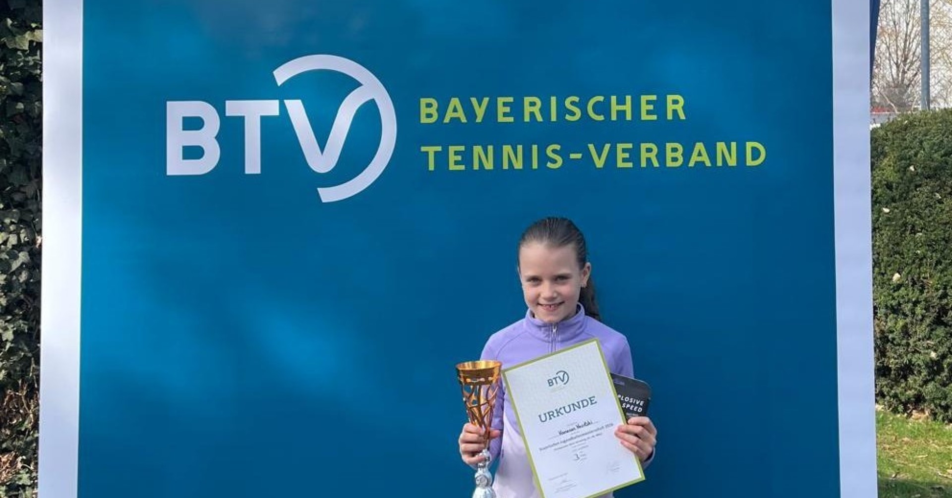 Vanessa bei der Bayerischen Meisterschaft 2026 mit Pokal und Urkunde vor dem Banner des Bayerischen Tennis-Verbands