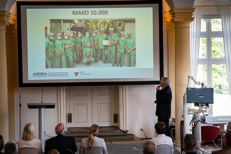 MAKO 10.000 Jubiläumspräsentation im Orthopädischen Krankenhaus Schloss Werneck mit Dr. Gerlach Präsentation zur MAKO 10.000 im Orthopädischen Krankenhaus Schloss Werneck mit Dr. Gerlach, Teamfoto vor Jubiläumszahl 10000