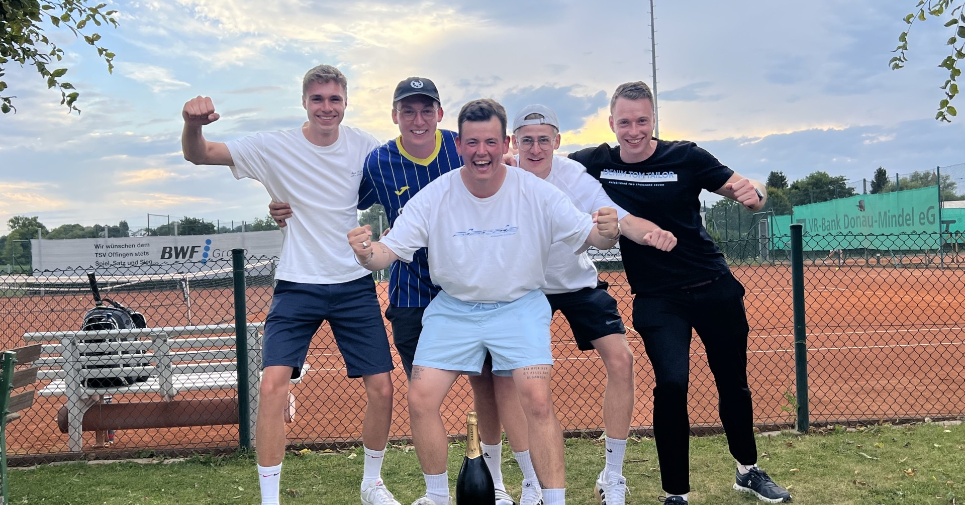 Team jubelt auf Tennisplatz mit Champagnerflasche Gruppe von jungen Männern auf einem Tennisplatz mit einer Champagnerflasche