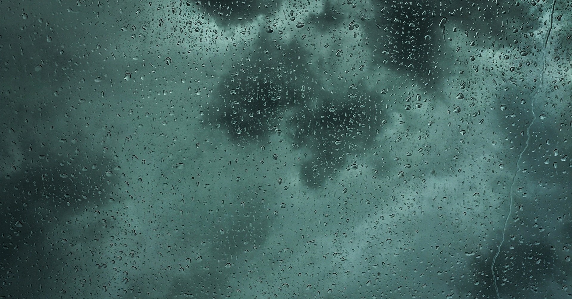 Regentropfen auf einem Fenster mit dunklen Wolken im Hintergrund