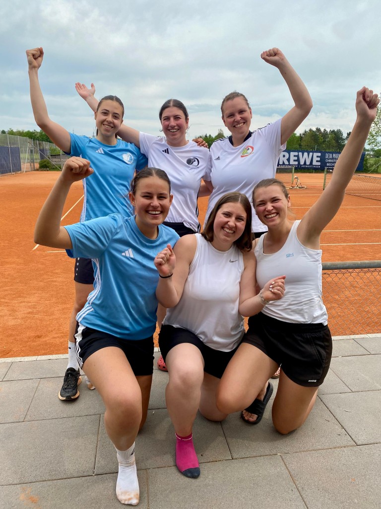 Gruppe junger Frauen jubelt auf Tennisplatz nach einem erfolgreichen Tennisspiel