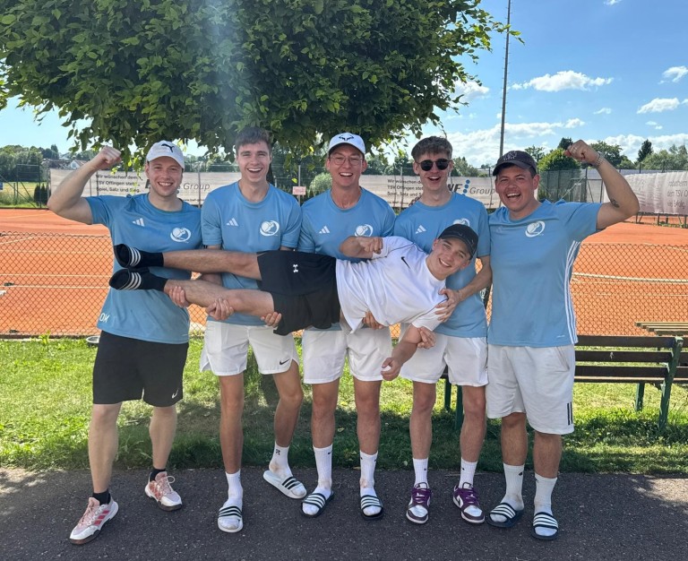 Tennis Herrenmannschaft posiert gemeinsam auf dem Tennisplatz, ein Spieler wird von den anderen getragen