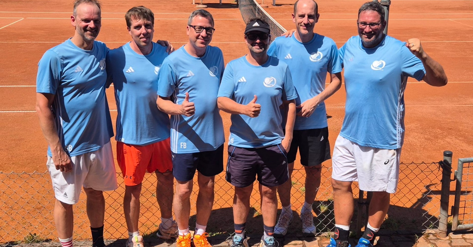 Sechs Männer im blauen Trikot auf einem Tennisplatz, Gruppenfoto bei sonnigem Wetter