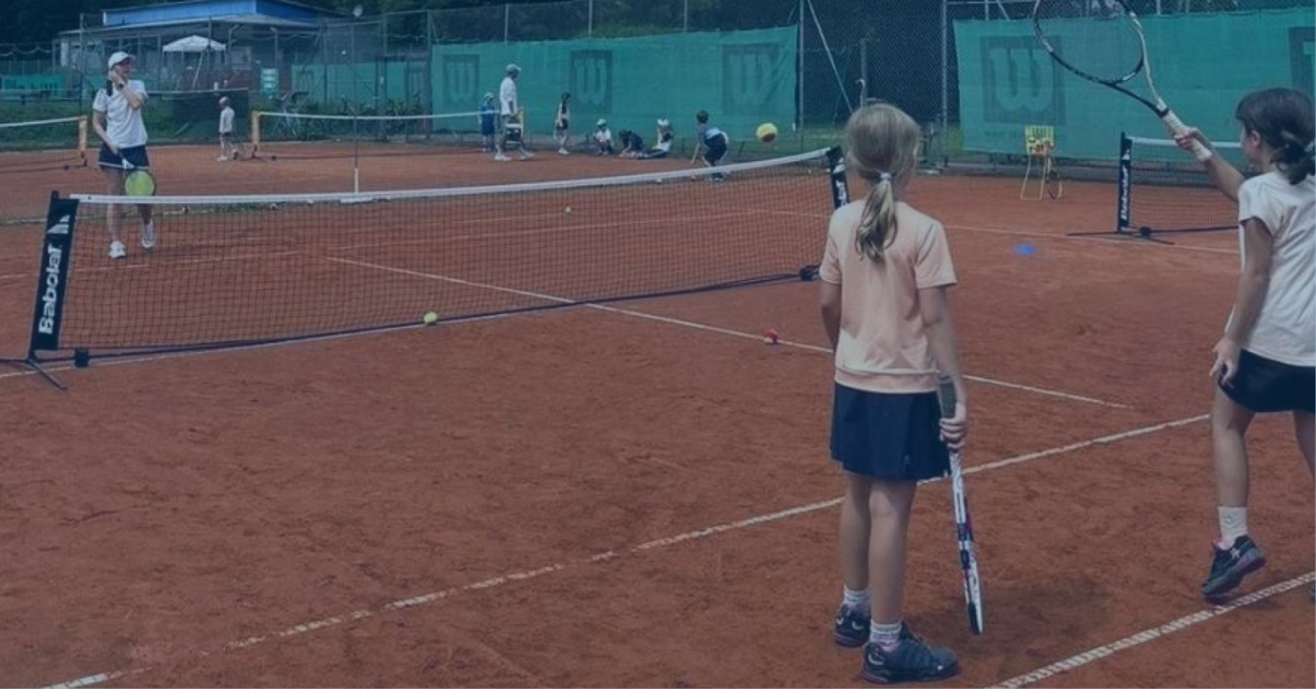 Kinder beim Tennisspielen im Sommerferiencamp auf einem Sandplatz