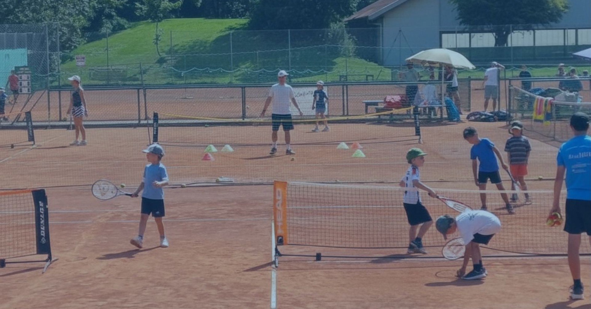 Kinder und Trainer beim Tennistraining auf dem Tennisplatz des TC WB, mit Netzen und Trainingshütchen