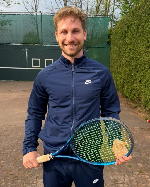 Lächelnder Mann im blauen Nike-Trainingsanzug mit Tennisschläger auf Tennisplatz
