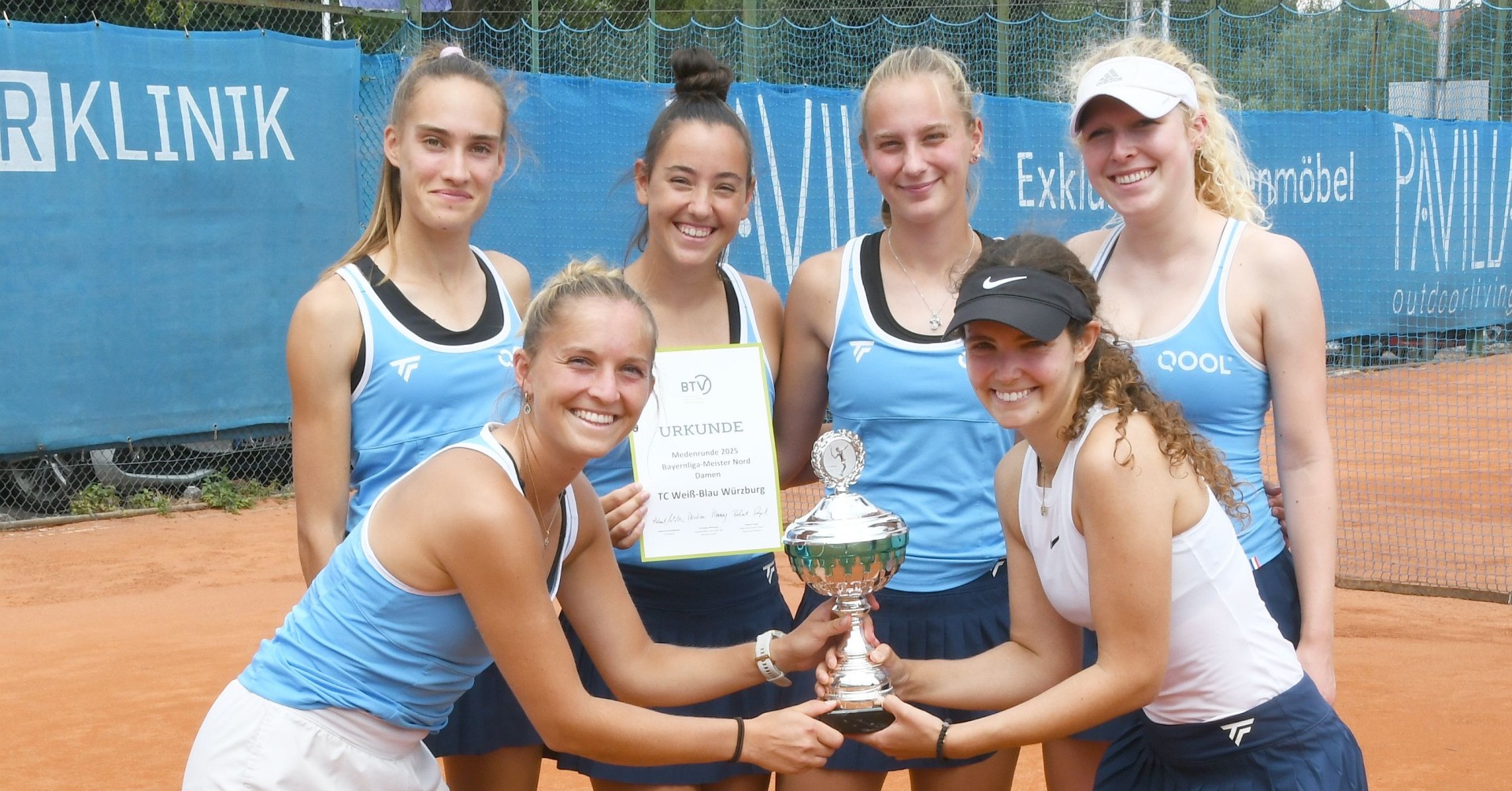Tennis-Team hält Pokal auf Sandplatz