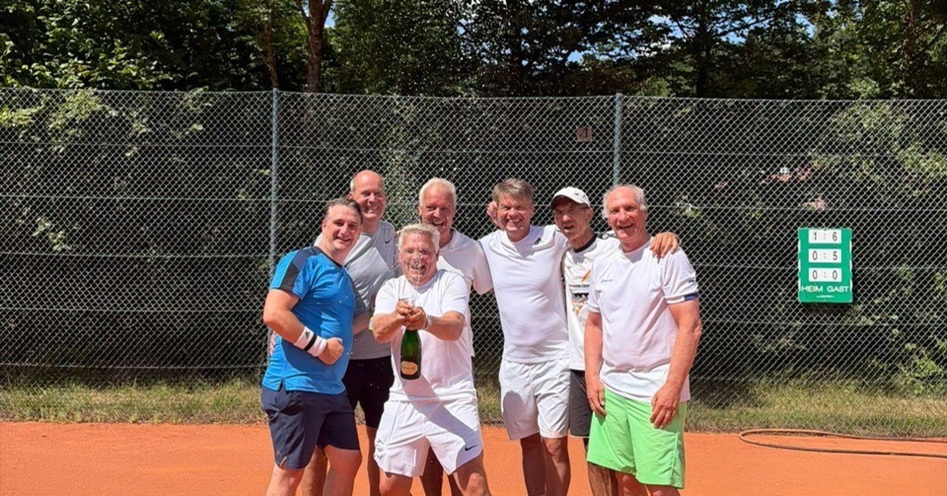 Herren 50 Tennismannschaft feiert auf Sandplatz mit Sekt nach einem Sieg