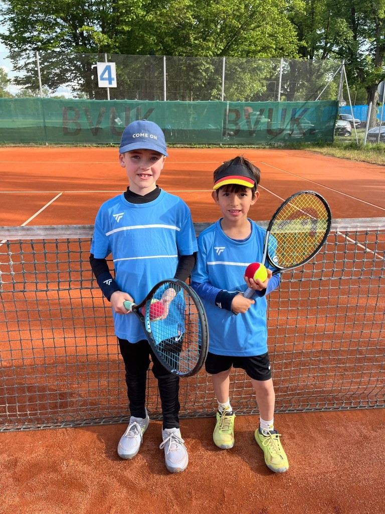 Zwei Kinder der U8-Tennis-Mannschaft auf einem Sandplatz mit Tennisschlägern und Tennisbällen