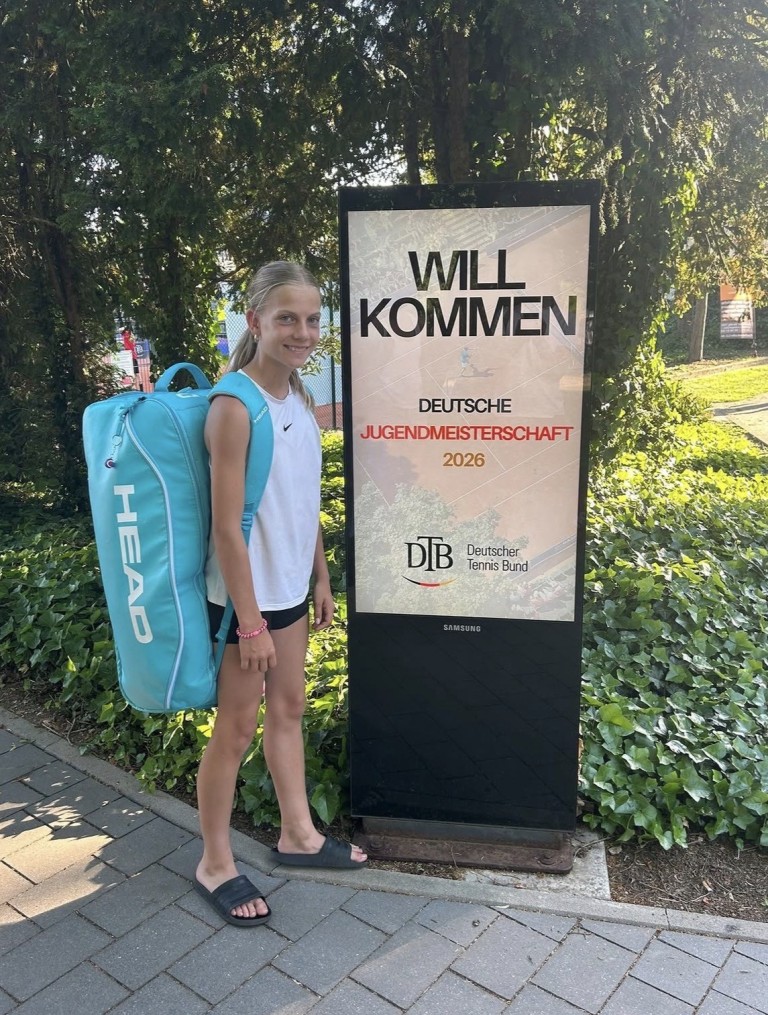 Junges Mädchen mit Tennistasche vor Begrüßungsschild zur Deutschen Jugendmeisterschaft 2026 des Deutschen Tennis Bundes (DTB)