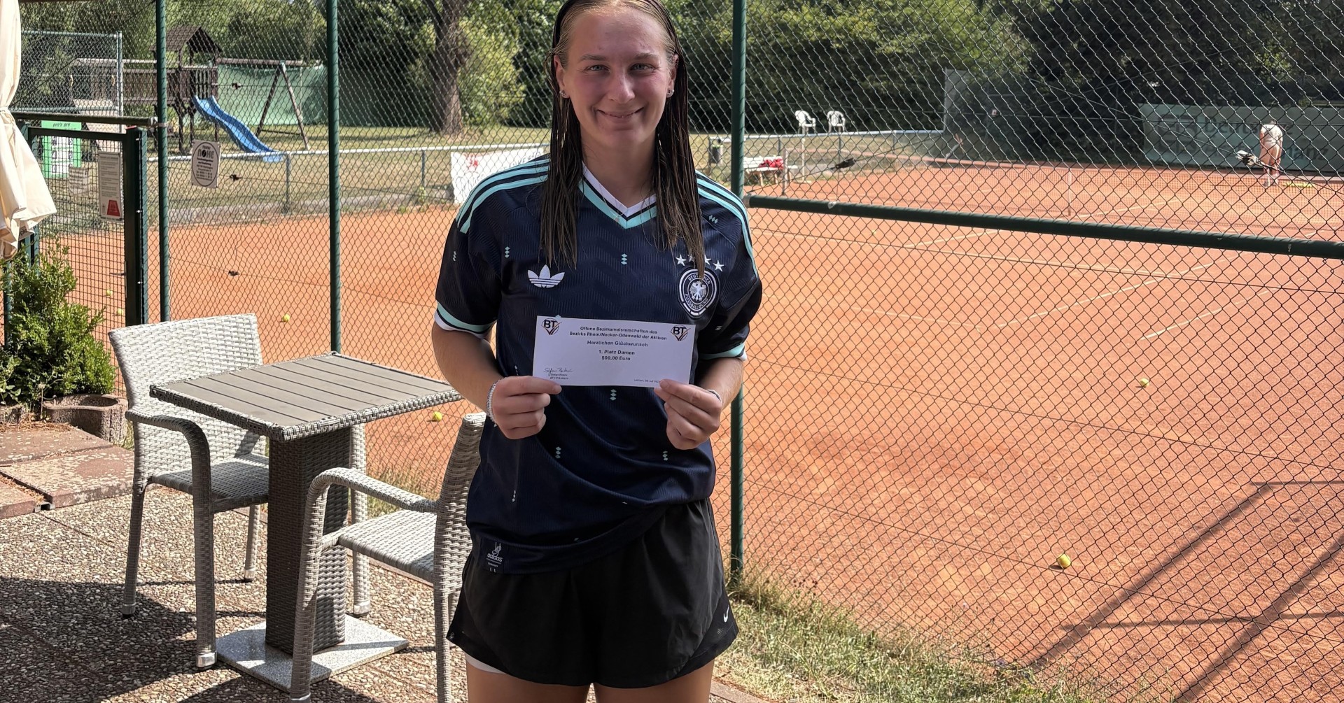 Josie auf einem Tennisplatz mit Urkunde in der Hand
