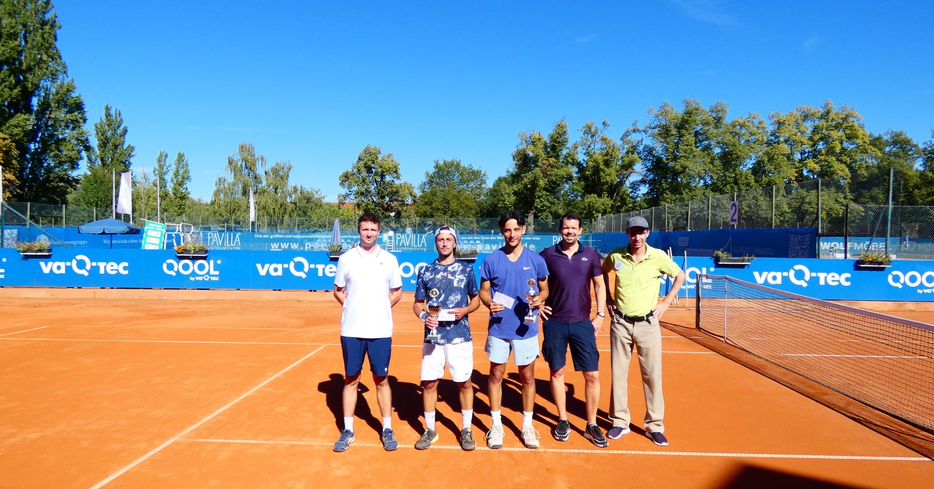 Gruppenfoto von fünf Männern auf einem Sand-Tennisplatz mit Pokalen, sonniges Wetter, Siegerehrung