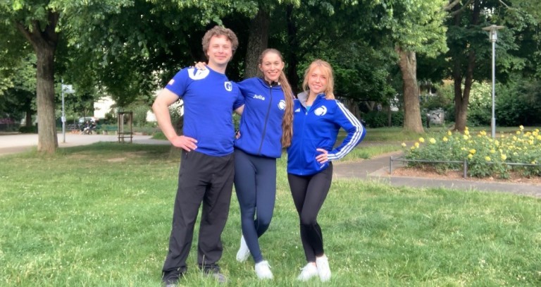 Drei Personen in blauer Sportkleidung stehen lächelnd auf einer Wiese im Park