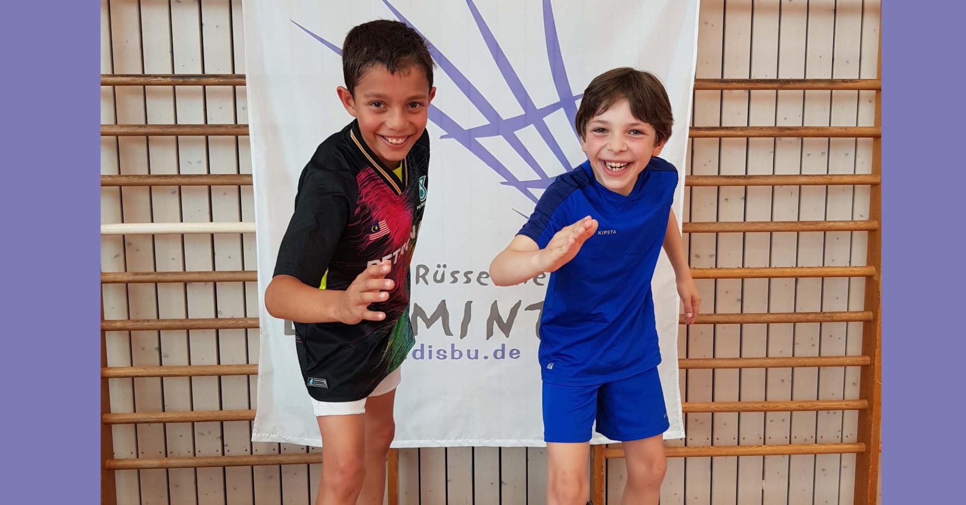 Zwei sportliche Jungen beim Lachen vor einem Banner in einer Turnhalle Zwei lachende Jungen in Sportkleidung vor einem Banner
