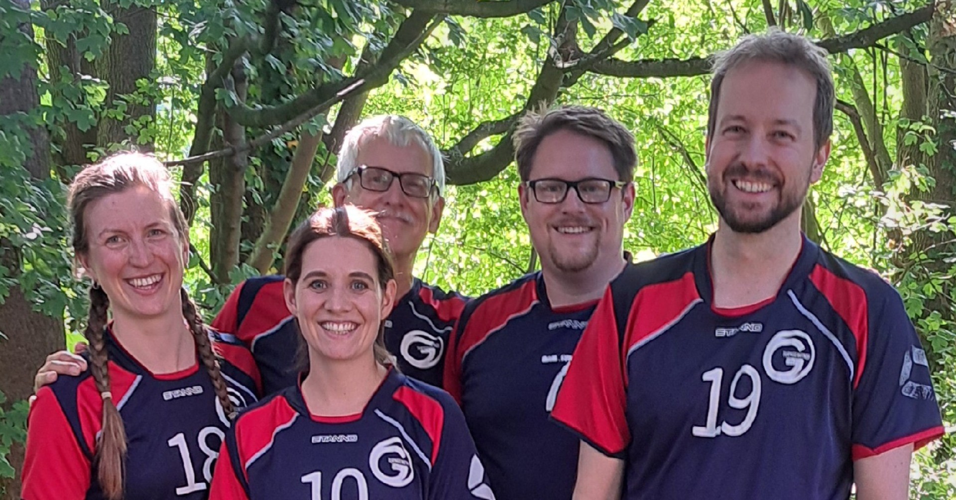 Volleyball-Teammitglieder im Freien Lächelnde Volleyball-Teammitglieder im Freien vor grünen Bäumen
