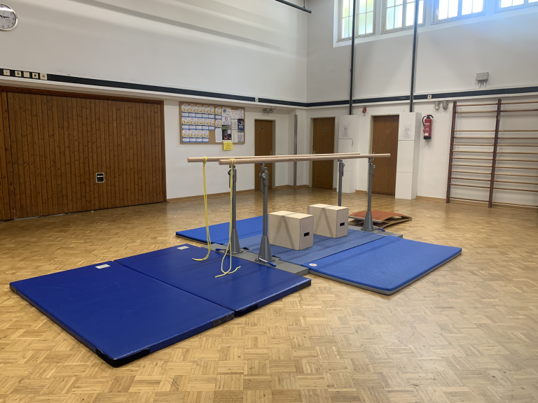 Parallelbarren in der Turnhalle – Turngerät für das Gerätturnen Parallelbarren in einer Turnhalle mit blauen Matten und Turngeräten