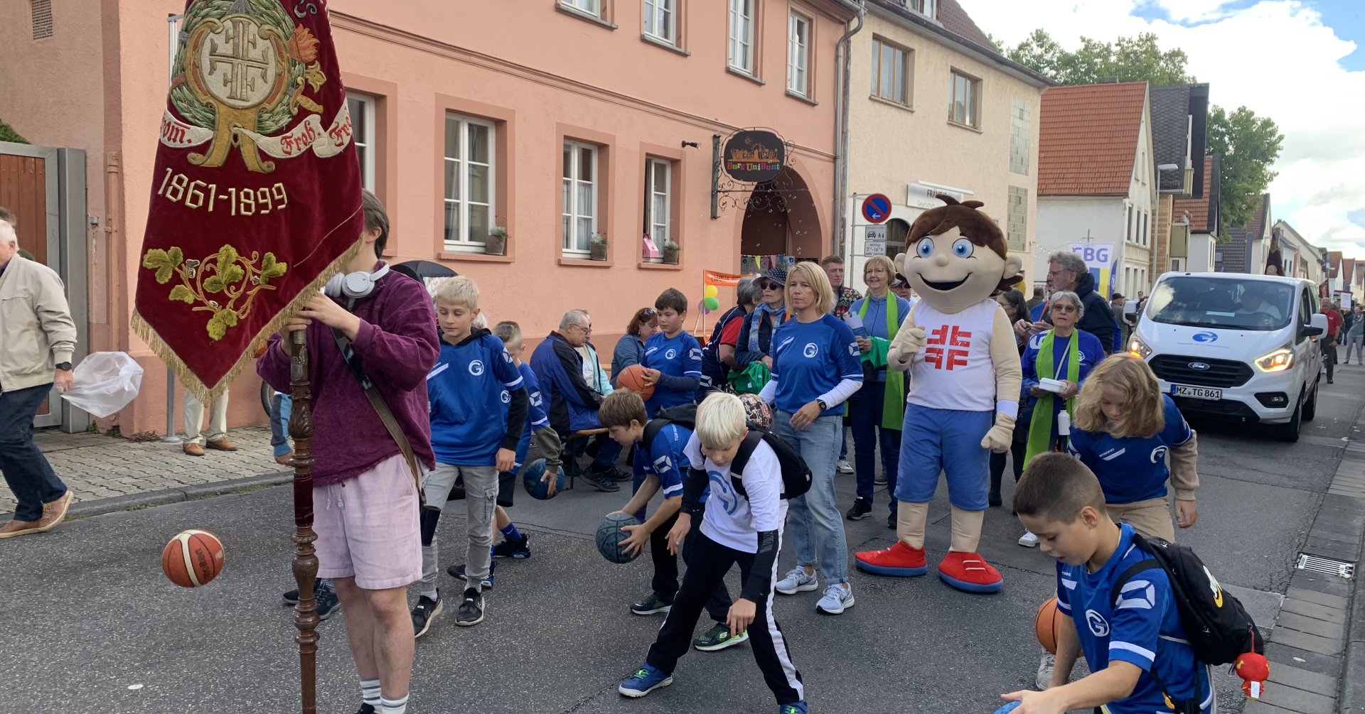 Kinder und Erwachsene in blauen Trikots mit Basketballen bei einem Festumzug in einer deutschen Stadt