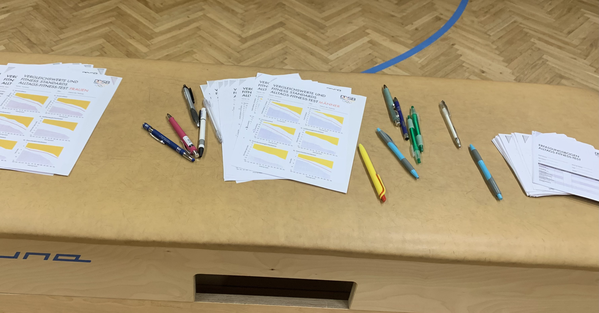 Unterlagen und Stifte zum DOSB Alltags-Fitness-Test (AFT) in einer Sporthalle