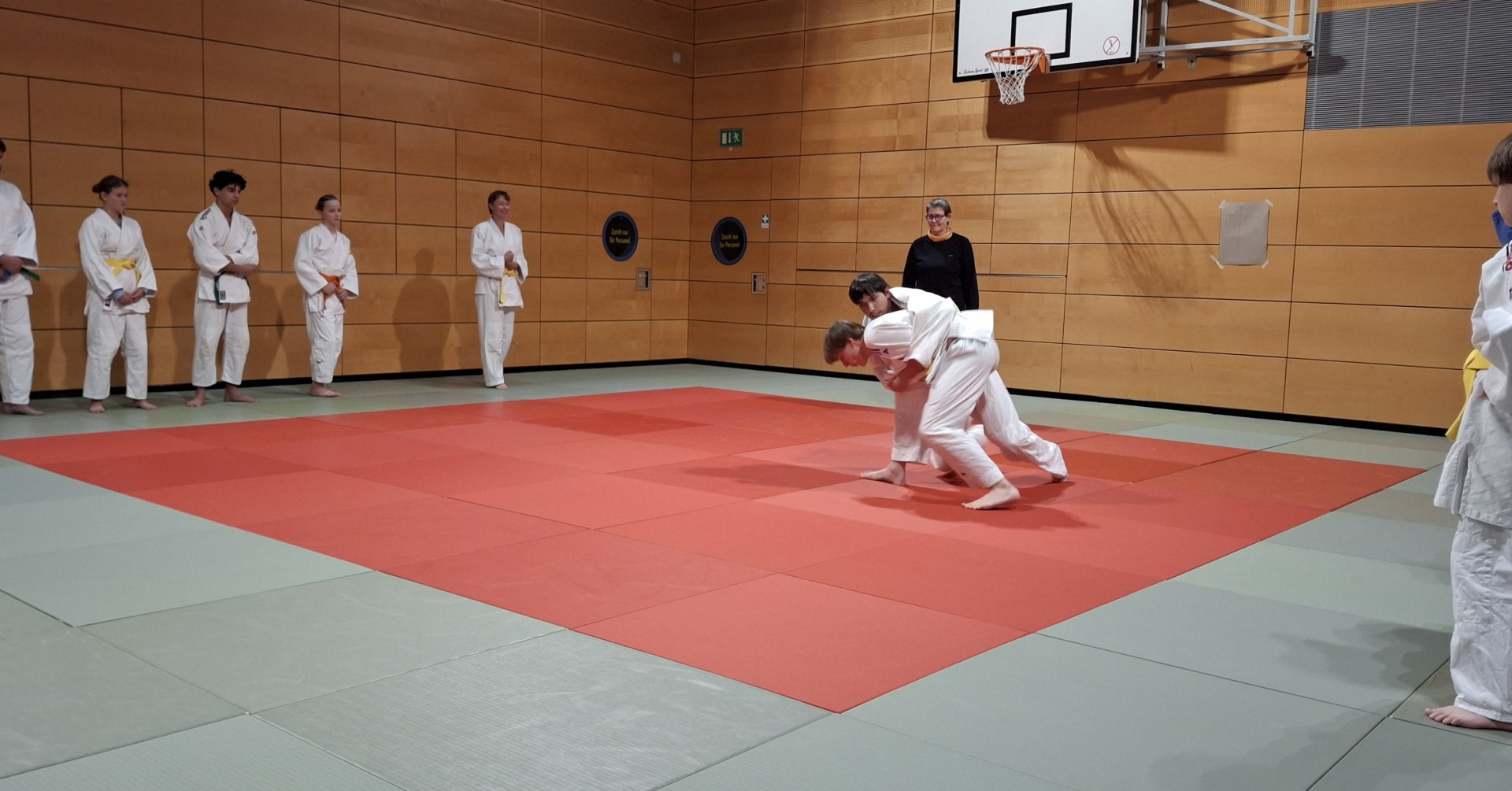 Judo Training in einer Sporthalle mit zwei Judoka beim Wurf auf roter Matte
