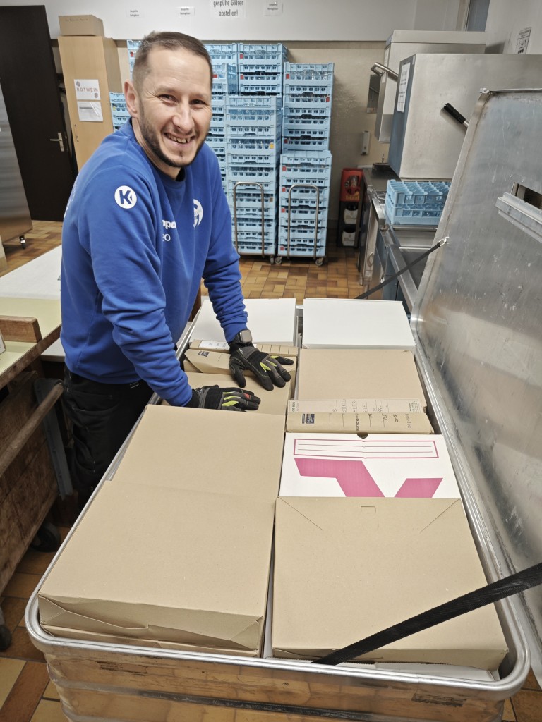 Mitarbeiter in blauer Arbeitskleidung sortiert Kartons in einem Lager oder Versandbereich