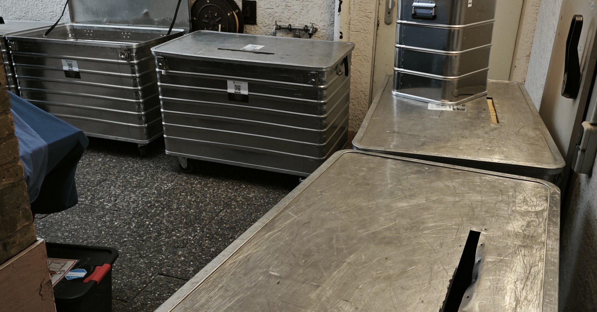 Mehrere große Metallkisten und Transportboxen in einem Hinterhof oder Lagerraum, geeignet für Transport oder Aufbewahrung