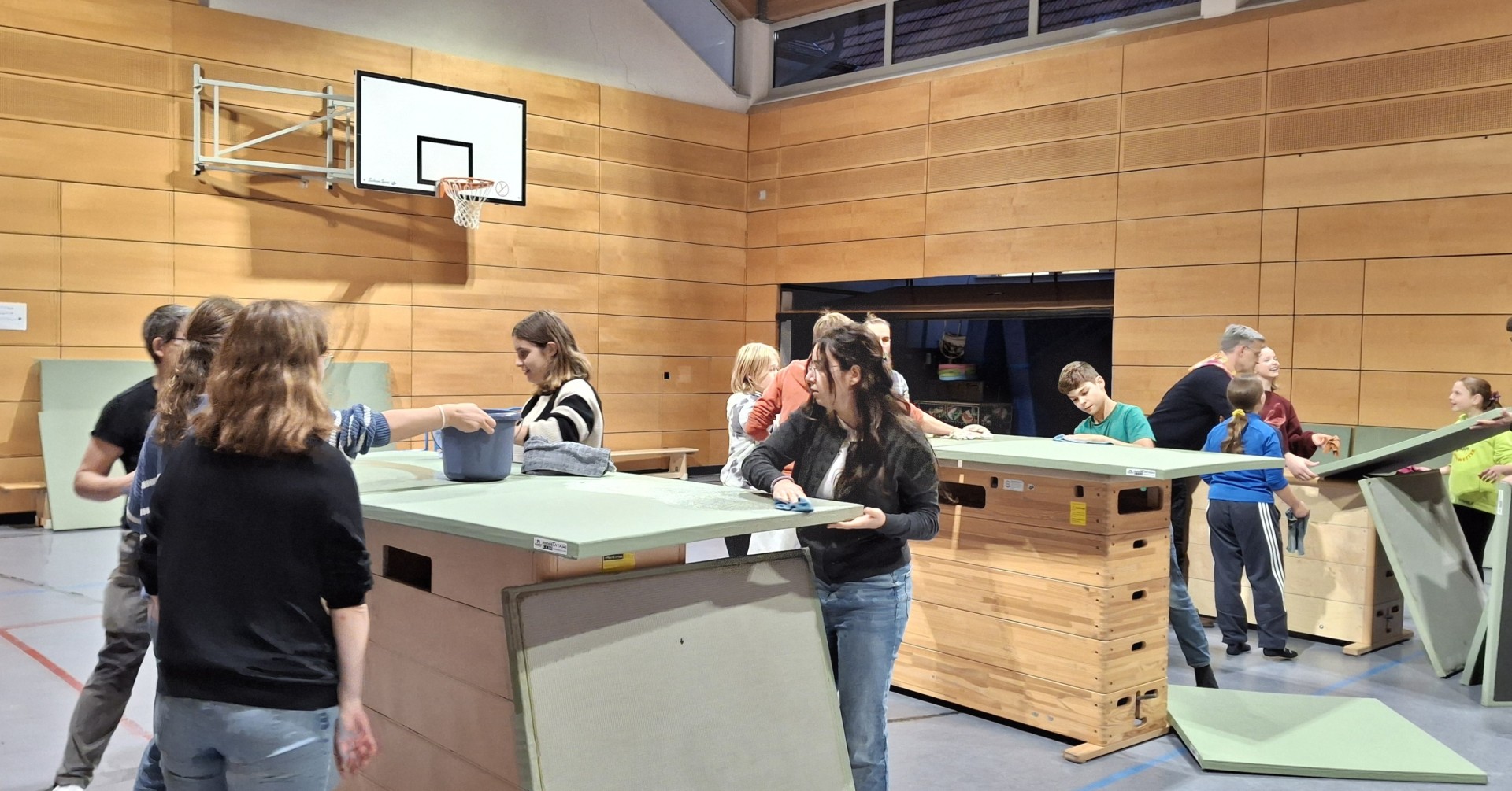 Mehrere Personen reinigen Turngeräte in einer Sporthalle