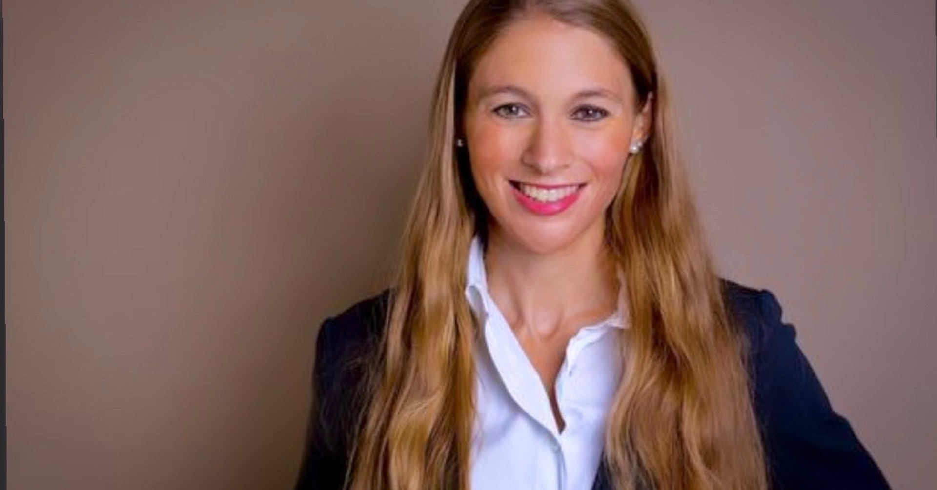 Frau mit langen blonden Haaren im Business-Outfit vor neutralem Hintergrund