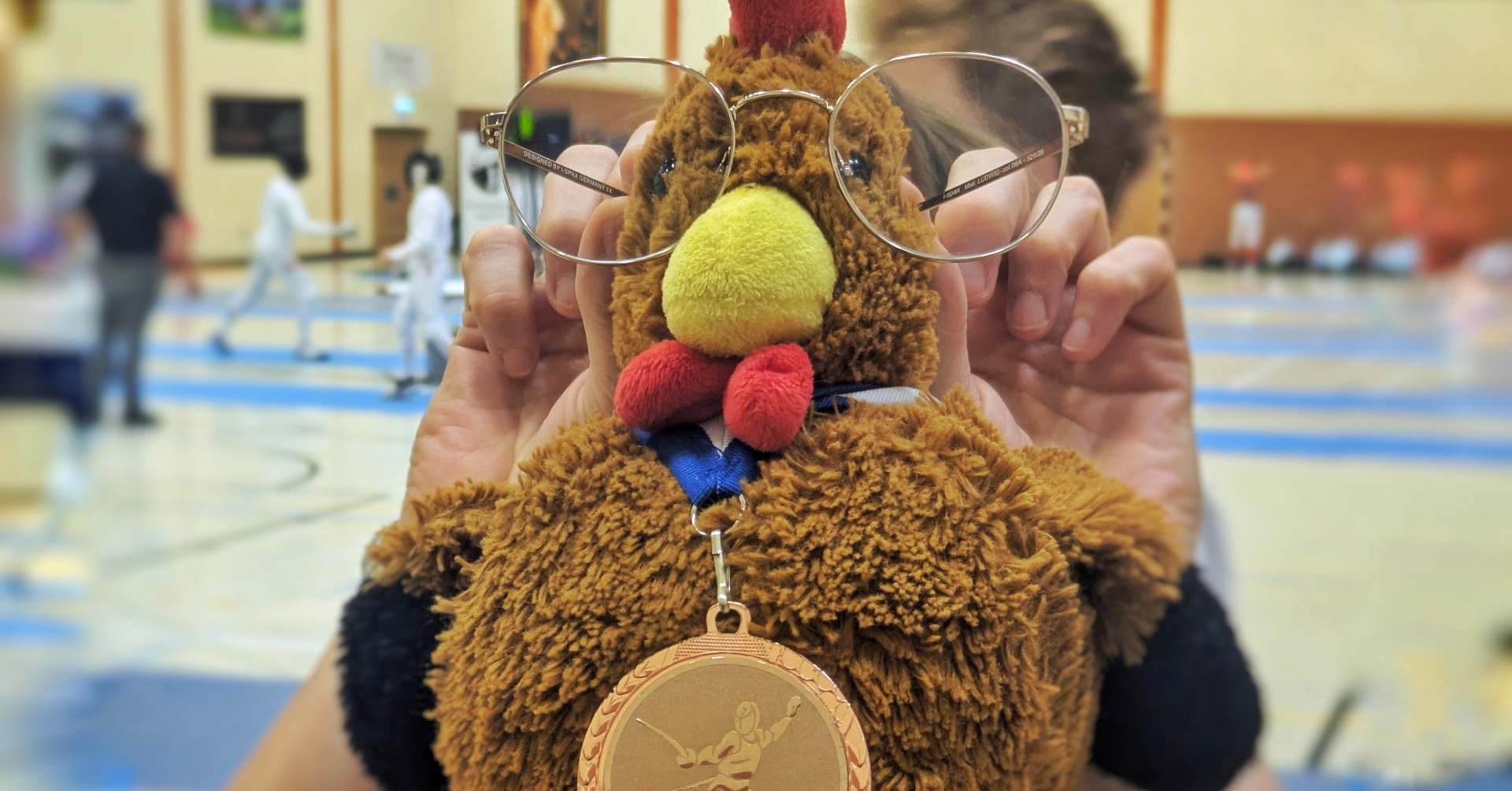 Plüschhuhn mit Brille und Fechtmedaille auf einem Fechtturnier Plüschhuhn mit Brille und Fechtmedaille bei einem Fechtturnier