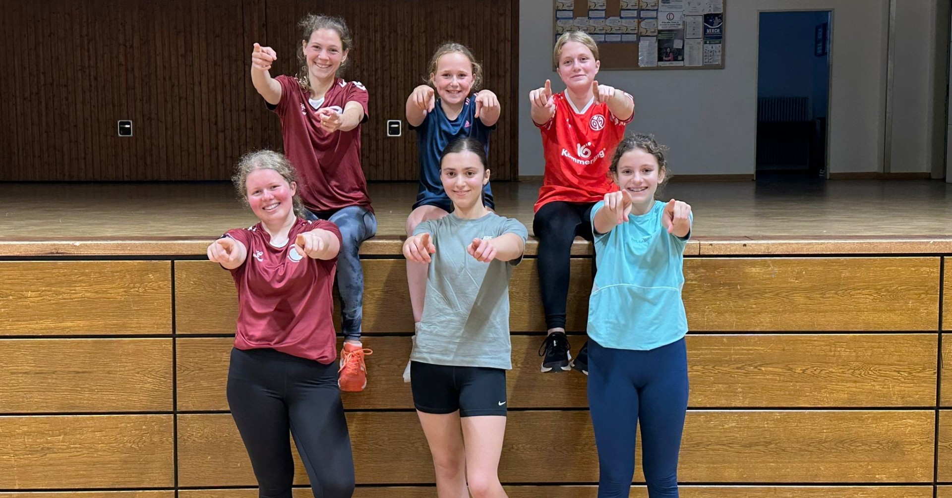 Jugendliche Sportgruppe in der Turnhalle beim gemeinsamen Training Gruppe von Jugendlichen beim Sport in einer Turnhalle, alle zeigen mit den Armen nach vorne