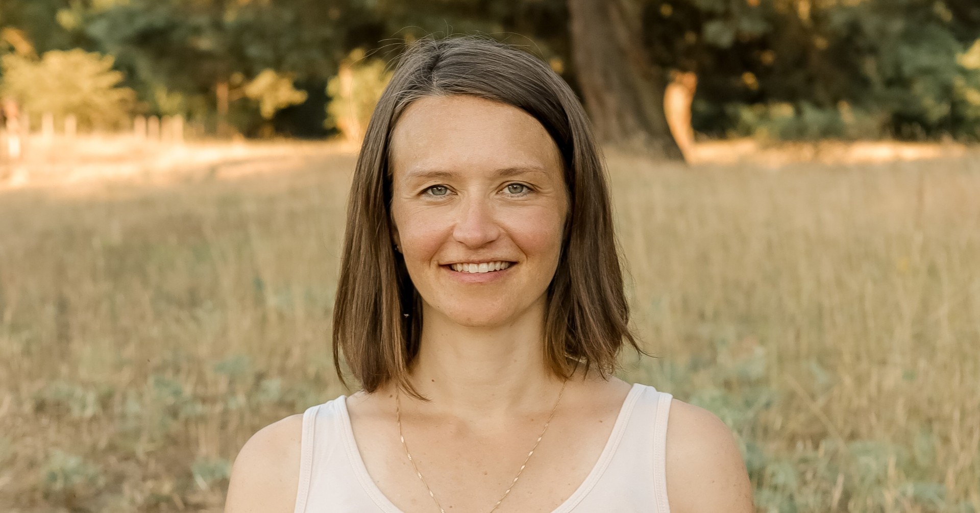 Frau mit braunen Haaren im ärmellosen Top auf einer Wiese vor Bäumen