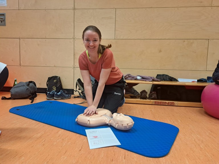 Herz-Lungen-Wiederbelebung (HLW) Training mit Reanimationspuppe im Erste-Hilfe-Kurs in Sporthalle Person übt Herz-Lungen-Wiederbelebung (HLW) an einer Reanimationspuppe während eines Erste-Hilfe-Kurses in einer Sporthalle