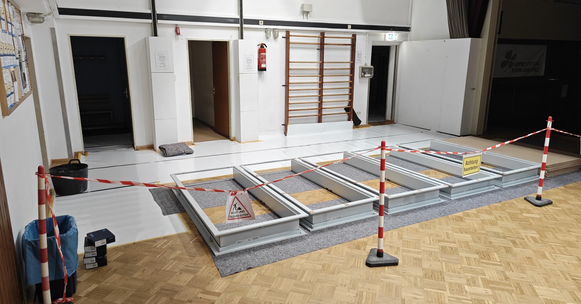 Baustelle in einer Turnhalle mit Absperrband und Warnschildern, Bodenarbeiten im Innenraum