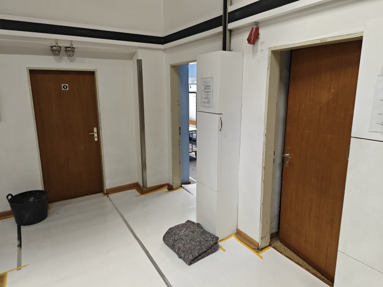 Flur mit zwei Holztüren, weißem Sicherungskasten und gefaltetem Umzugsdecke auf dem Boden