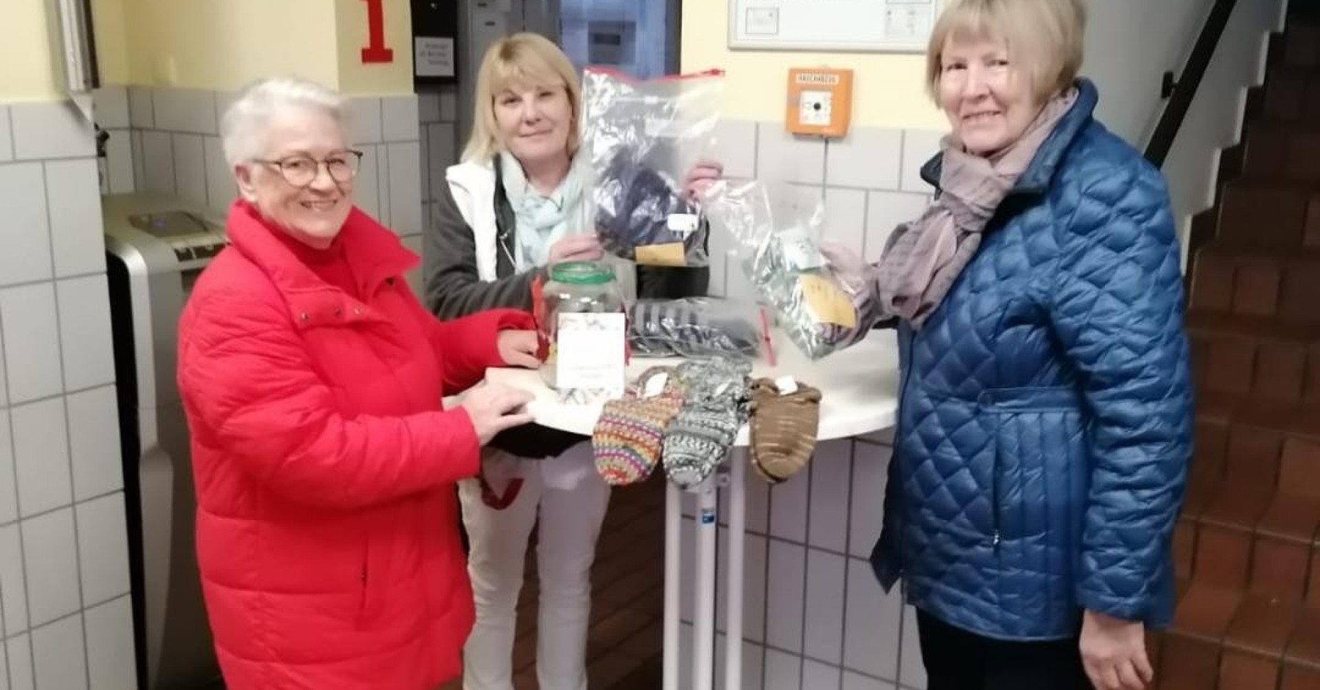 Drei Frauen präsentieren handgestrickte Socken auf einem Tisch im Eingangsbereich, socken-2025
