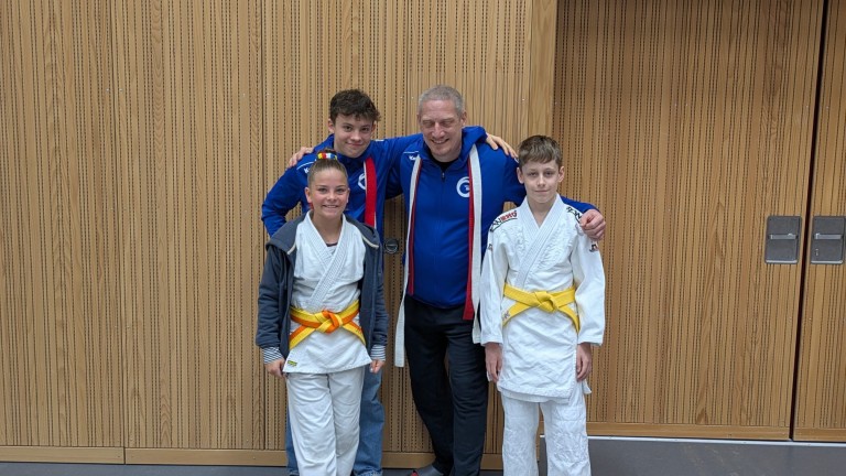 Judo-Trainer mit zwei jungen Judoka im weißen Judoanzug und gelbem Gürtel bei einem Turnier