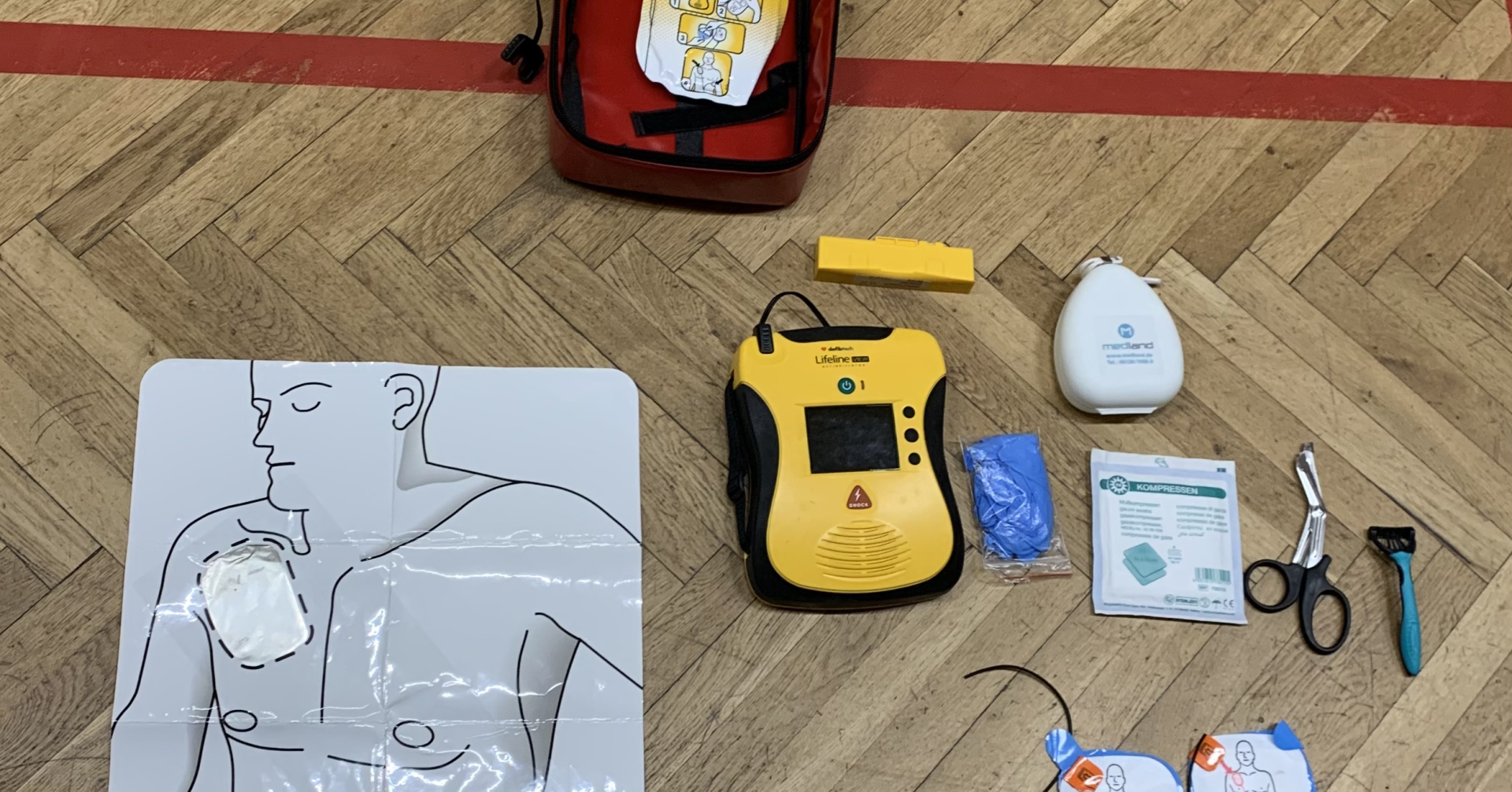 Defibrillator-Einweisung mit Übungspuppe, AED-Gerät und Zubehör auf Turnhallenboden