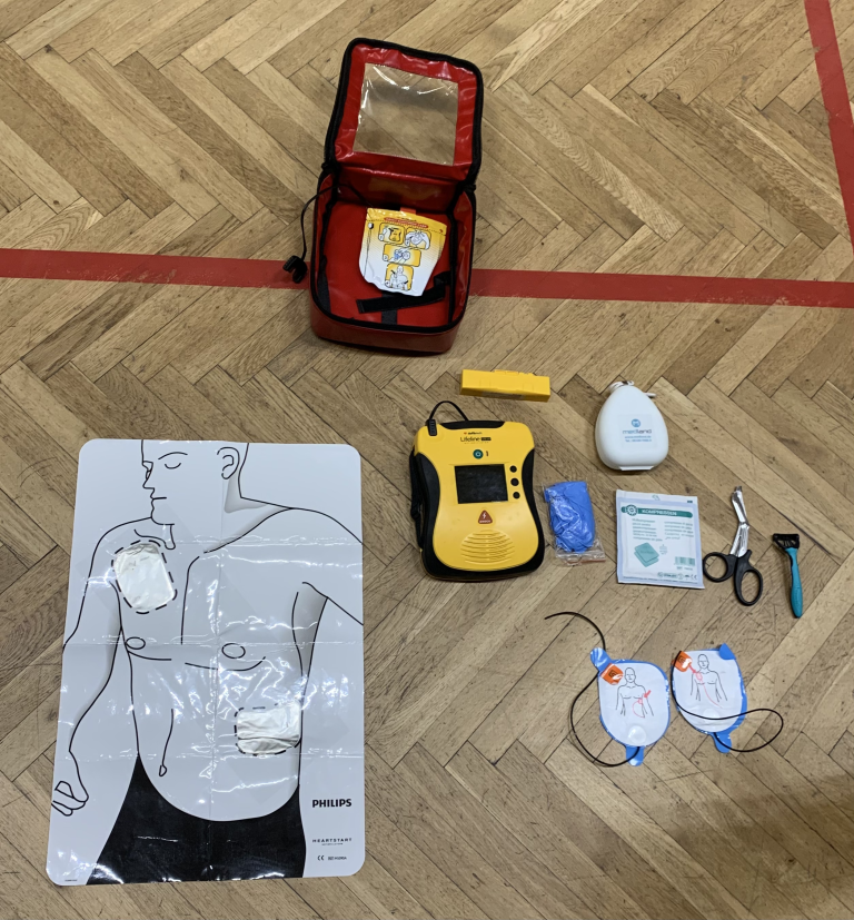 Defibrillator-Einweisung mit Übungspuppe, AED-Gerät und Zubehör auf Turnhallenboden