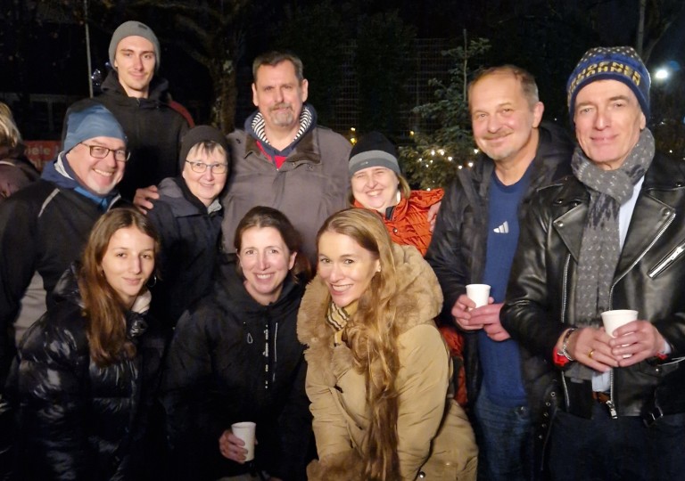 Gruppe von Menschen beim Adventsmarkt 2025, draußen am Abend mit festlicher Beleuchtung