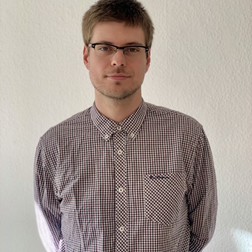 Angel Ponow mit kariertem Hemd vor weißer Wand