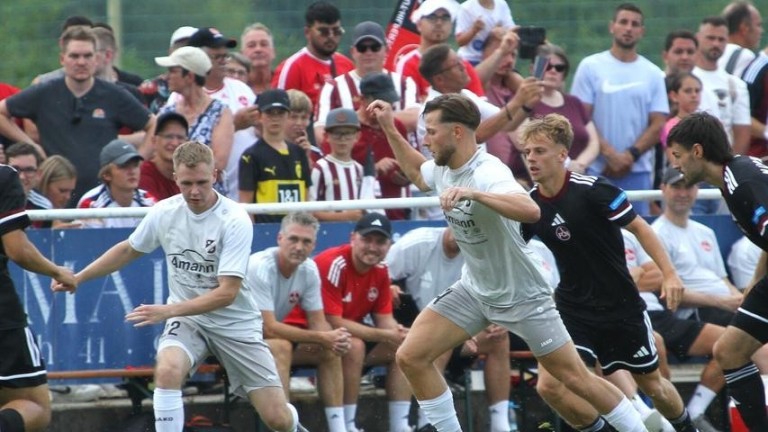 Spannende Spielsituation bei einem Fußballspiel vor begeistertem Publikum Fußballspiel mit Spielern in weißer und schwarzer Kleidung vor Zuschauern