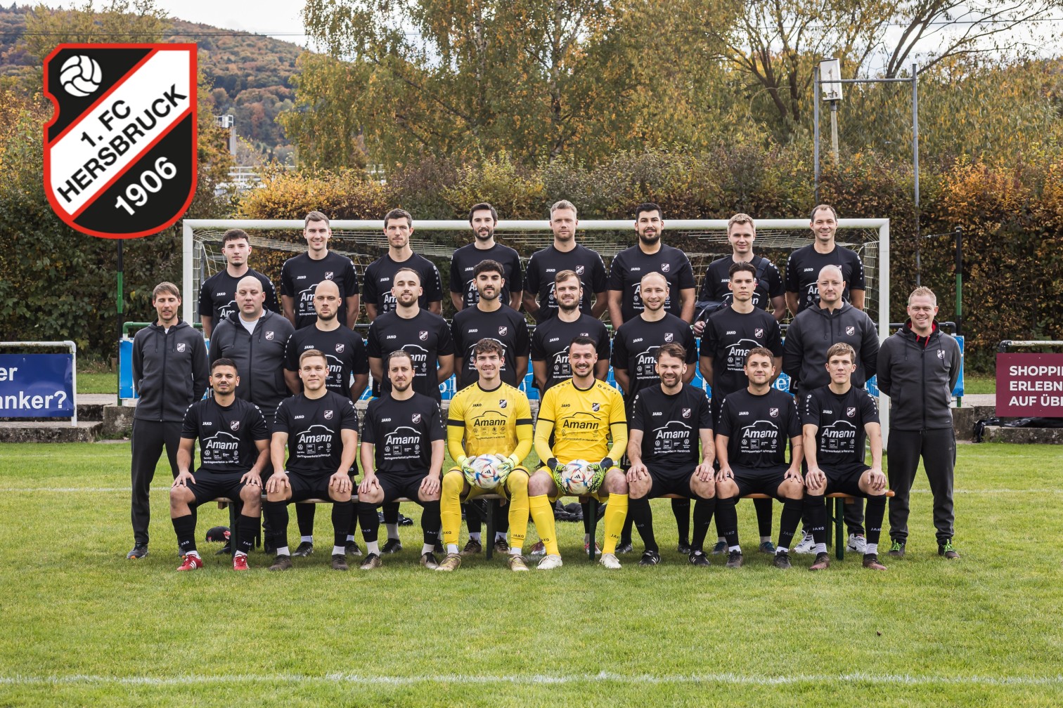 Mannschaftsfoto eines Fußballteams in schwarzen Trikots mit Amann-Werbung, aufgenommen vor einem Tor auf einem Fußballplatz