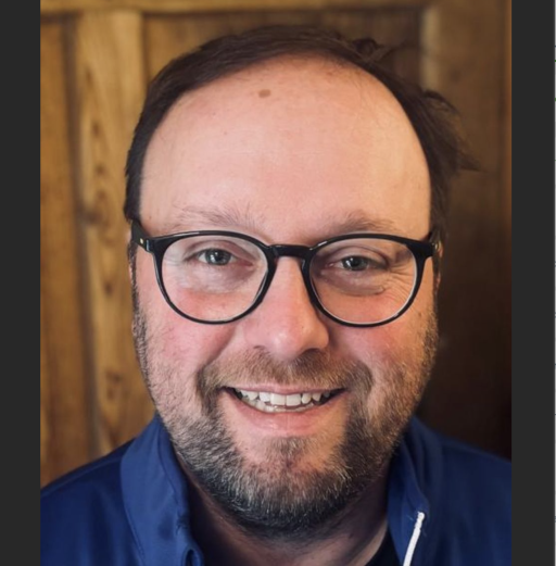 Bildschirmfoto vom 3. November 2025 um 10:42:35, Person vor Holz-Hintergrund in blauem Hemd