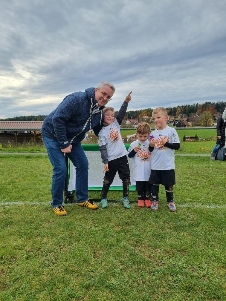 Kinder beim Fußballspiel im Freien mit Trainer auf dem Sportplatz, Herbstlandschaft im Hintergrund