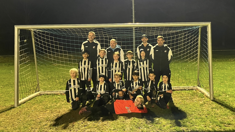 Jugend-Fußballmannschaft in schwarz-weißen Trikots vor einem Tor auf einem Fußballplatz bei Nacht