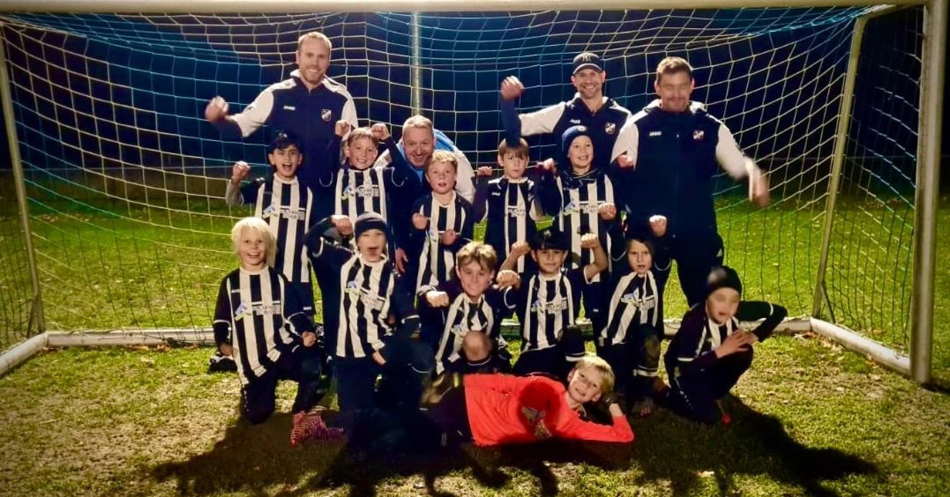 Kinderfußballmannschaft mit Trainern vor einem Tor auf dem Fußballplatz bei Nacht