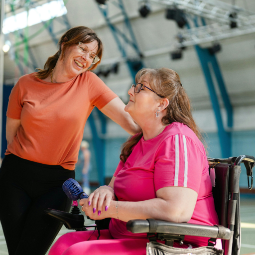 Zwei Frauen beim Sport in einer Halle, eine davon im Rollstuhl, inklusive Sportaktivität, Symbolbild für Inklusion und Barrierefreiheit, ow2025-sb-50