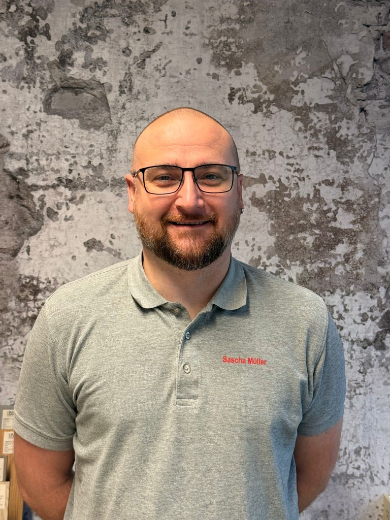 Sascha Müller mit grauem Poloshirt vor grauer Wand