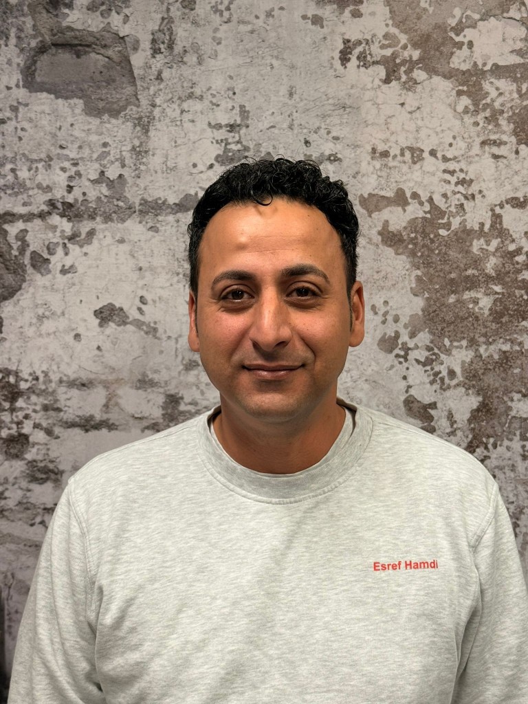 Esref Hamdi vor einer Wand mit grauer Struktur, Porträtaufnahme