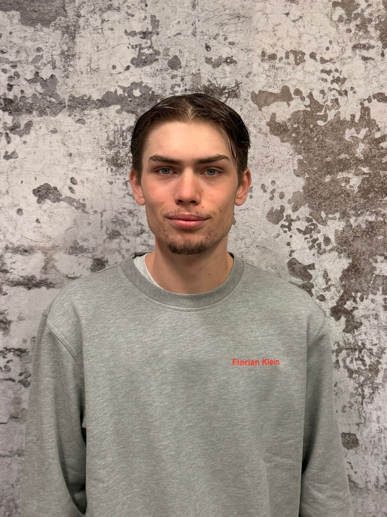 Person mit grauem Pullover und rotem Schriftzug Florian Klein vor Betonwand