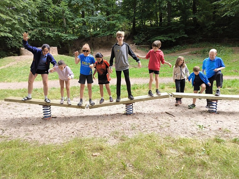 Kinder beim Balancieren auf einer Wippe im Outdoor-Spielplatz Kinder spielen gemeinsam auf einer Balancierwippe im Freien auf einem Spielplatz